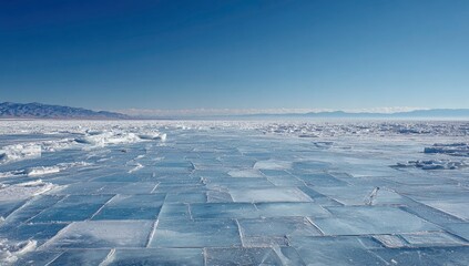 Obraz premium Frozen lake landscape, vast ice blocks, clear sky, distant mountains; winter scene