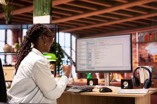 Smiling coder at workstation programming on computer, celebrating after successfully writing lines of code. Woman in home office pleased after managing to debug software before deadline