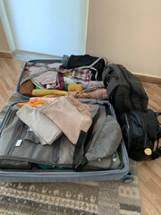 Open suitcase with neatly folded clothes, ready for trip, suitcase is placed on floor near wardrobe in room