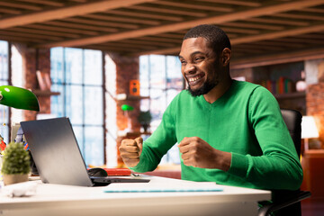 Approving joyful man at home happily shaking fists, ecstatic about accomplishments. Excited african...