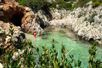 A stunning view through foliage of a man enjoying the pristine waters of a secret beach in Zante, Greece. This picture evokes a sense of paradise found, adventure, and exclusive travel.