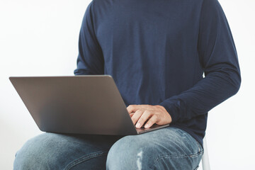 Young man typing on laptop while sitting in chair, white background. Remote work, online learning, freelance business concept. Online education technology, entrepreneur, digital social communication.