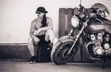 biker sitting next to motorcycle in urban setting