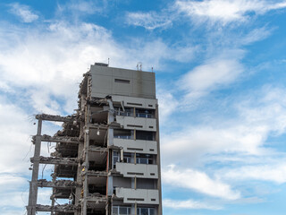Building demolition reveals a partially destroyed structure under a blue sky with clouds