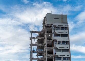 Building demolition process under a cloudy sky reveals stark structural remnants of modern...