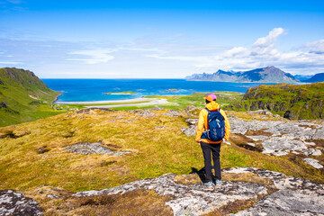 Obraz premium Female hiker enjoys spectacular view over mountains and Yttersand beach from trail to Ryten, Lofoten Islands, Norway