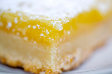 Extreme close-up of a tangy lemon bar with a golden shortbread crust and a dusting of powdered...