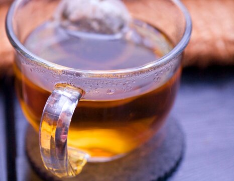 A close-up shot of a steaming cup of herbal tea in a clear glass mug on a dark coaster, capturing the rich amber hue of the liquid. Perfect for themes of wellness, relaxation, and comfort.