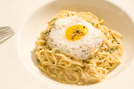 A sophisticated plate of creamy pasta topped with a frothy egg yolk center, garnished with black pepper.