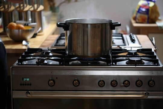 A steaming stainless steel pot sits on a lit gas burner in a warm, lived-in kitchen.
