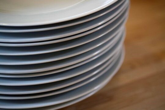 A vertical close-up of neatly stacked white ceramic plates on a wooden countertop, capturing the order and calm of a kitchen setting.