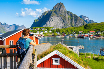 Female hiker taking picture of spectacular view of Reine village with sea and mountains, Lofoten...