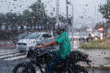 A motorcyclist  is seen through a glass window with raindrops during a rainy day in São Paulo, Brazil.
