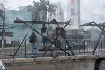 People are seen through a glass window with raindrops taking shelter from the rain at a bus stop during a storm in Sao Paulo, Brazil.