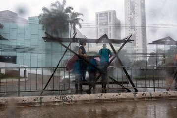 People are seen through a glass window with raindrops taking shelter from the rain at a bus stop in Sao Paulo, Brazil.