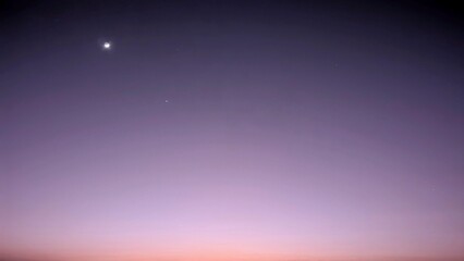 A sunrise sky displaying a gradient of soft purples, blues, and faint orange at the horizon, with a...