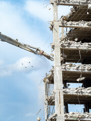Demolition of a high-rise building underway at a construction site with clear blue sky in the...