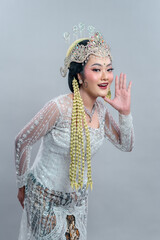 A graceful Indonesian bride in Sundanese traditional attire smiles warmly while leaning forward in...