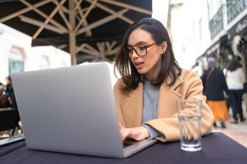 Woman, digital nomad working remotely from a cafe, drinking water and using laptop, smiling.