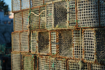 Several crab traps are stacked together in a coastal area as the sun sets in the background,...