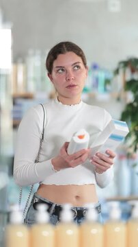Girl in summer clothes choosing skin cream at the drugstore. High quality 4k footage
