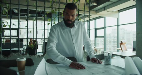 An architect is meticulously reviewing and analyzing blueprints in a modern, innovative workspace - Powered by Adobe