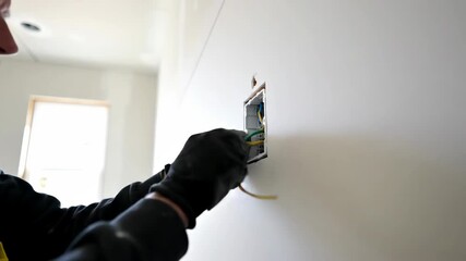 Electrician installing wall outlet, connecting grounding wire for electrical safety during home renovation.