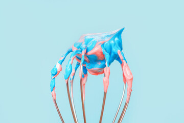 Whisk with whipped cream from proteins close-up on blue background.