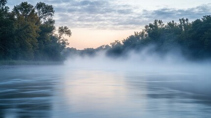 Fototapeta premium A serene river landscape unfolds with ethereal fog blanketing the water, framed by lush trees under a soft, cloudy sky, creating a tranquil and atmospheric vista.