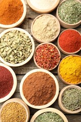 Different aromatic spices in bowls on wooden table, flat lay