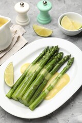 Tasty cooked asparagus served with sauce and lime on grey textured table, closeup