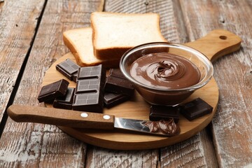 Tasty chocolate butter in glass bowl, pieces, bread and knife on color wooden table, closeup