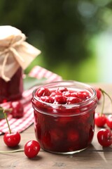 Tasty cherry jam and fresh fruits on wooden table against blurred background, closeup. Space for text