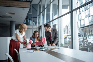 Businesswoman receiving gifts and flowers from colleagues in office