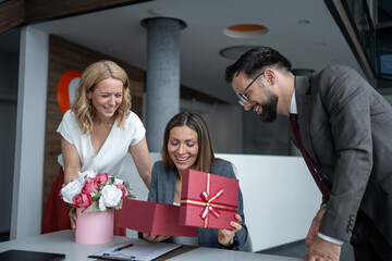 Businesswoman opening a gift box surrounded by colleagues