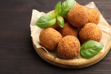 Delicious fried croquette balls with basil on wooden table, closeup