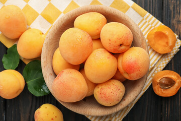 Fresh wet apricots in bowl and green leaves on wooden table, flat lay