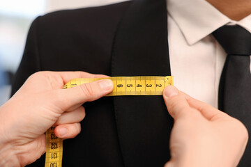 Tailor measuring jacket on man in atelier, closeup