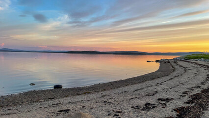  Evening landscape with lakeshore and soft blue-pink sky. Still water reflects fading daylight, creating a serene mood of natural silence and balance.