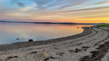  Evening landscape with lakeshore and soft blue-pink sky. Still water reflects fading daylight,...