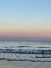 Fototapeta premium sunset over the sea with small waves crashing in the water without a cloud in the sky