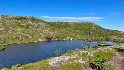 Quiet mountain lake in Murmansk Oblast, Russia. Surrounded by rocky green hills and under a bright blue sky — a serene spot in the Russian Arctic wilderness.