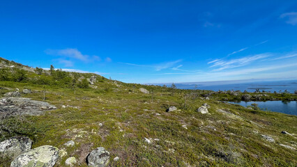Rocky northern landscape near a lake in Murmansk Oblast, Russia. Summer day with clear blue skies and scattered clouds. Wild, untouched nature.