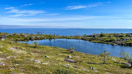 A wooden trail on the Kola Peninsula, Murmansk Oblast, Russia, leads to a scenic mountain lake surrounded by tundra hills and untouched northern wilderness.