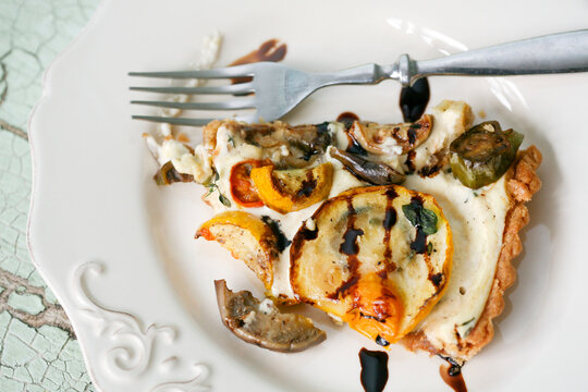 A rustic slice of grilled vegetable tart topped with zucchini, tomatoes, and mushrooms, drizzled with balsamic glaze.
