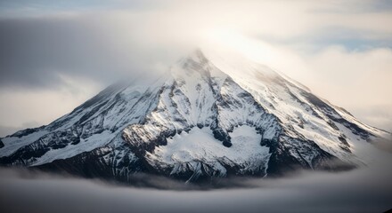 A majestic snowcapped mountain peak emerges from swirling clouds and mist, creating a dramatic natural landscape