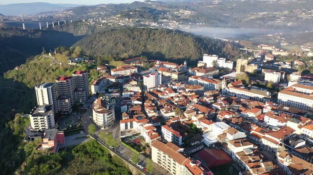 Picturesque drone view of Vila Real cityscape in valley framed by Alvao and Marao mountain ranges in light fog with suspension viaduct crossing Corgo River in background on sunny spring day, Portugal