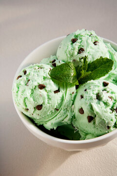 Close-up of creamy mint chocolate chip ice cream scoops in a white bowl, garnished with fresh mint leaves.