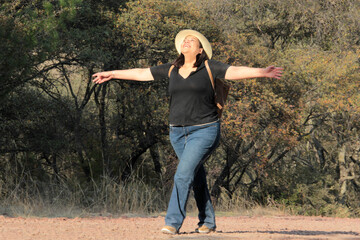 A 40-year-old Latina woman hikes in the mountains to fully enjoy nature and sunlight, experiencing well-being and empowerment