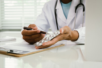 A doctor consults with a patient, explaining medical documents at a desk with a clipboard, laptop,...